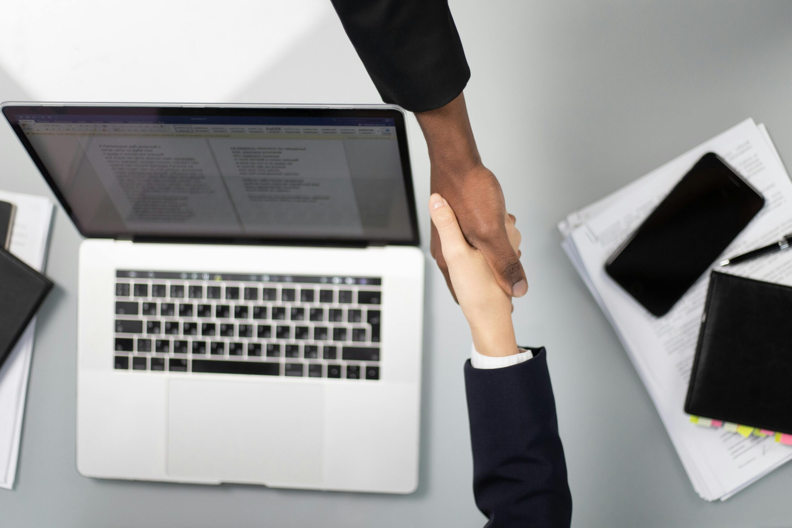 Overhead view of a professional handshake over a laptop, symbolizing business agreement.